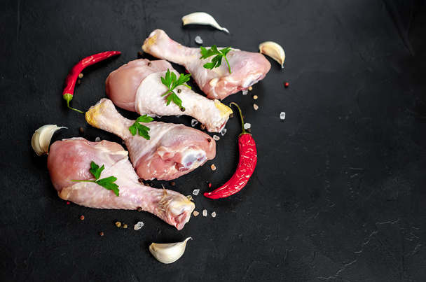 Chicken legs with spices, chili peppers and parsley leaves on black stone background - Photo, Image