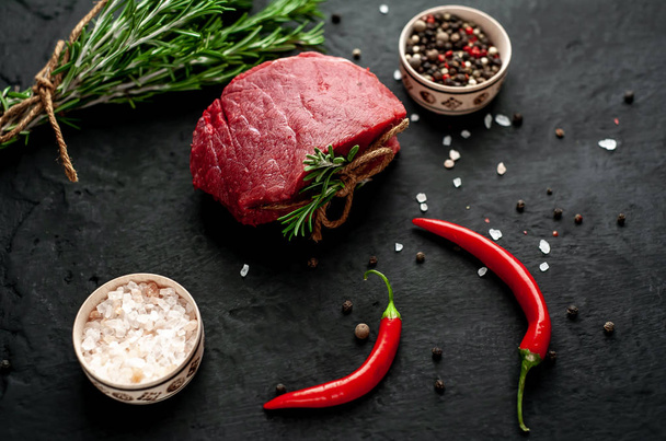 Surový steak se zelenými rozmarýznými větvičky a kořením na černém kamenném pozadí  - Fotografie, Obrázek