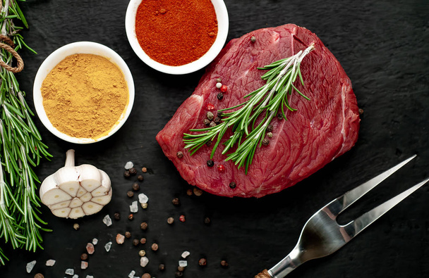 Nyers friss steak, fűszerek, fekete kő háttér - Fotó, kép