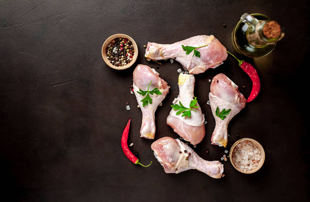 Pernas de frango com especiarias, sal, azeite e folhas de salsa sobre fundo de pedra preta
 - Foto, Imagem