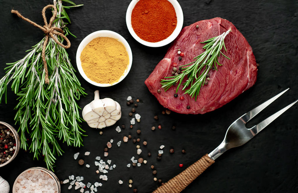 Raw fresh steak with spices on black stone background - 写真・画像