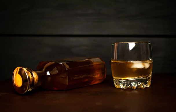 Glass of whiskey with ice cubes and whiskey bottle on black background  - Photo, Image