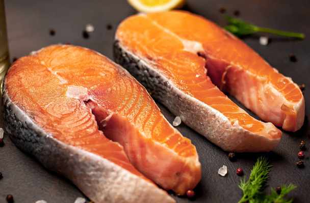 Fresh raw salmon steaks with spices and lemon on black stone background - Photo, Image