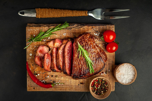Свежий говяжий стейк с помидорами, перцем чили и розмарином на деревянной доске
 - Фото, изображение