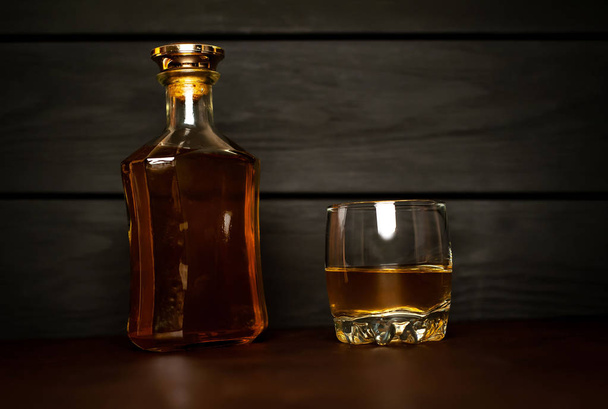 Glass of whiskey with ice cubes and whiskey bottle on black background  - 写真・画像