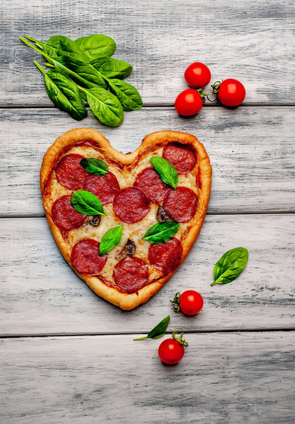 cheese heart pizza with salami, fresh basil leaves and ripe cherry tomatoes on wooden background  - Photo, Image