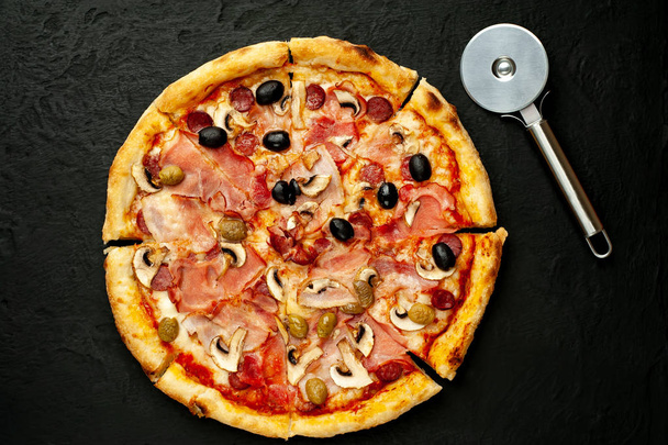 frische hausgemachte Pizza mit Pilzen, Tomaten, Oliven und Schinken auf schwarzem Stein Hintergrund - Foto, Bild