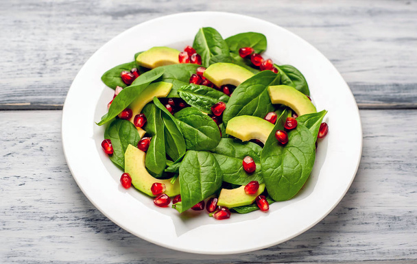 frischer grüner Salat mit Spinatblättern, Avocadoscheiben und Granatapfelkörnern auf Holztisch  - Foto, Bild