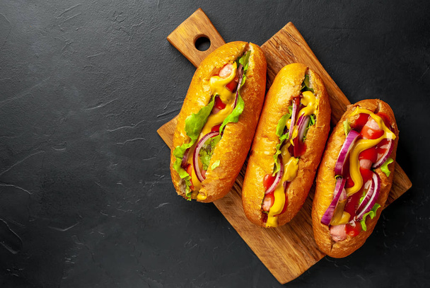 Verse zelfgemaakte hotdogs met groenten en sauzen op houten plank  - Foto, afbeelding