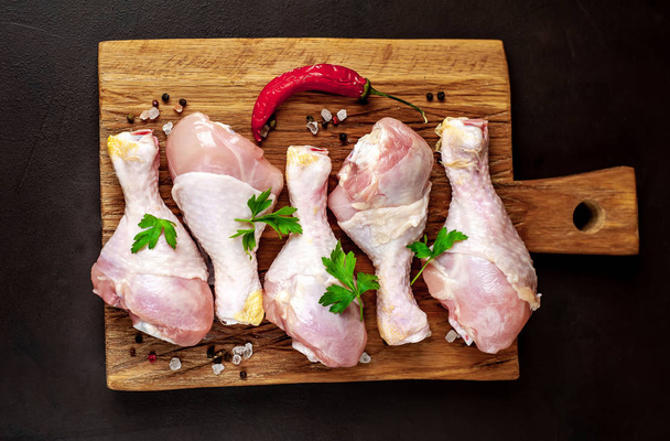 Chicken legs with spices,salt, chili pepper and parsley leaves on wooden board over black stone background - Photo, Image