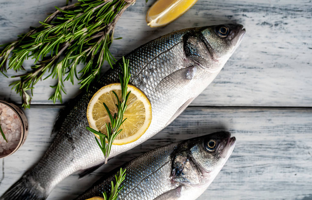 Raw fish with lemon slices and rosemary twigs on grey wooden background - Φωτογραφία, εικόνα