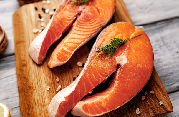 Bistecche fresche di salmone crudo con spezie su tagliere di legno
 - Foto, immagini