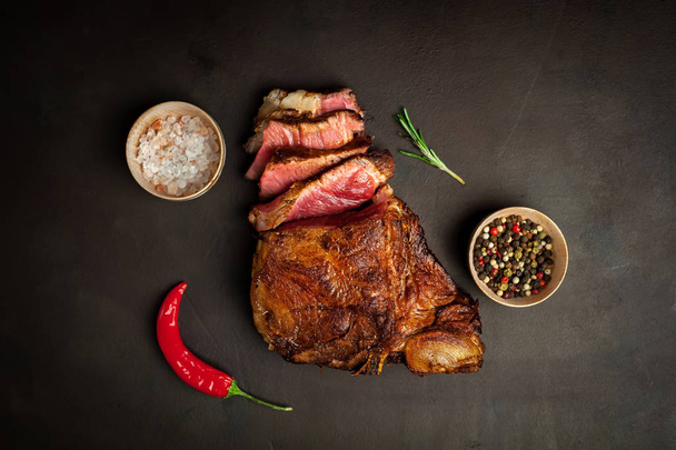 Fatty grilled pork steak with spices and chili pepper on black stone background - Photo, Image