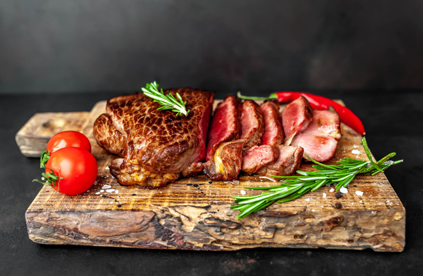 Fresh juicy medium rare beef steak served with chili pepper and rosemary twigs on wooden board - Photo, Image