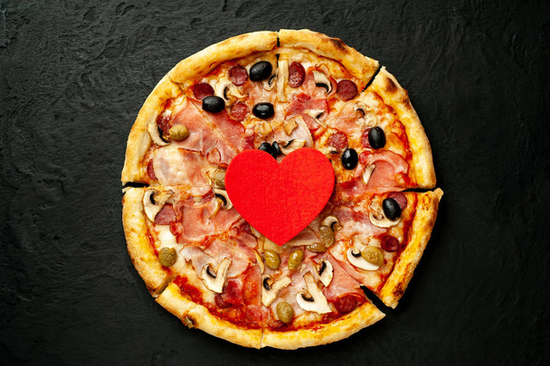 Свежая домашняя пицца с грибами, помидорами, оливками и ветчиной с красным сердцем на фоне черного камня
 - Фото, изображение