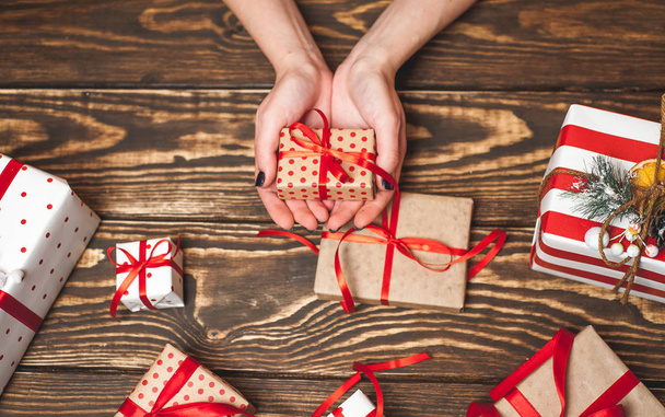 Female hands decorating gift boxes with red bows on old wooden background  - Photo, Image