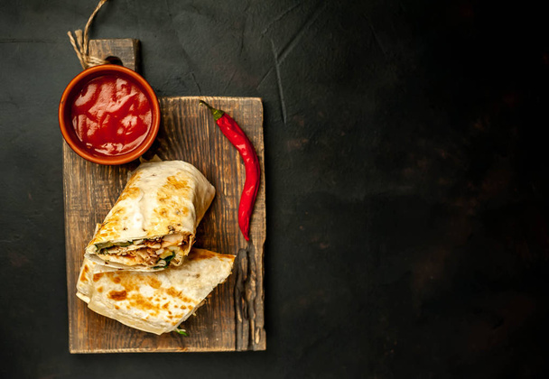 Tradiční Mexická burrito obalená kuřecím masem a zeleninou s pikantní omáčkou na dřevěné sekací prkno  - Fotografie, Obrázek