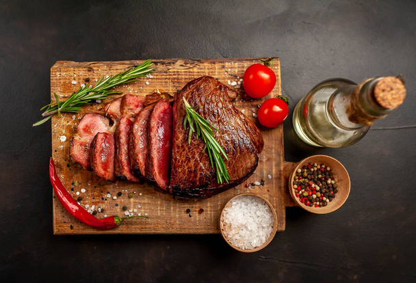 Fresh juicy medium rare beef steak served with chili pepper and rosemary twigs on wooden board - Photo, Image
