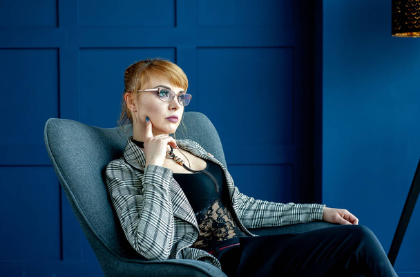 Элегантная деловая женщина, сидящая в кресле в голубой студии
  - Фото, изображение