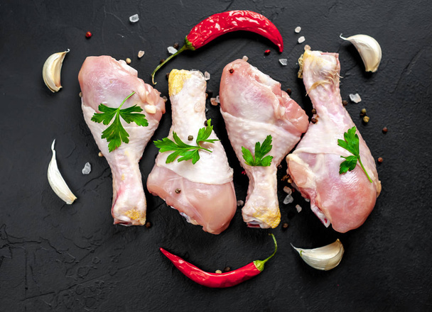 Chicken legs with spices, chili pepper and parsley leaves on black stone background - Foto, Bild