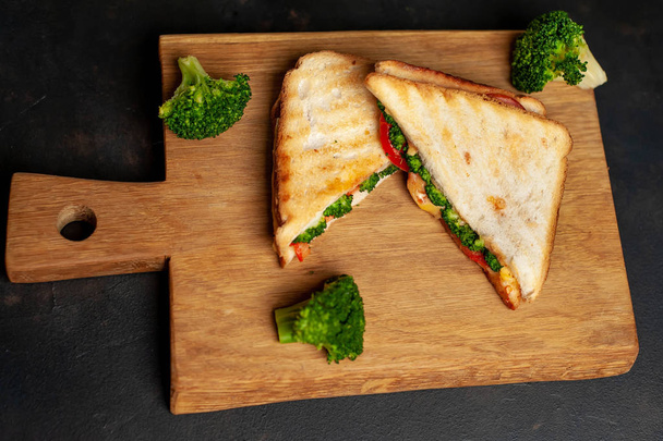 Sandwiches frescos a la parrilla con jamón, brócoli fresco y queso sobre tabla de cortar de madera
 - Foto, Imagen