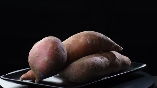 Zoete aardappelen draaiend op een zwart dienblad. Ipomoea Batatas - Video