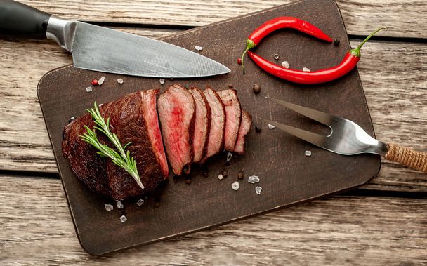 Fresh grilled steak with spices and rosemary twigs on wooden background - Photo, Image