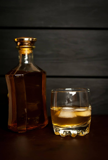 Glass with icy whiskey and bottle on dark wooden background  - Φωτογραφία, εικόνα