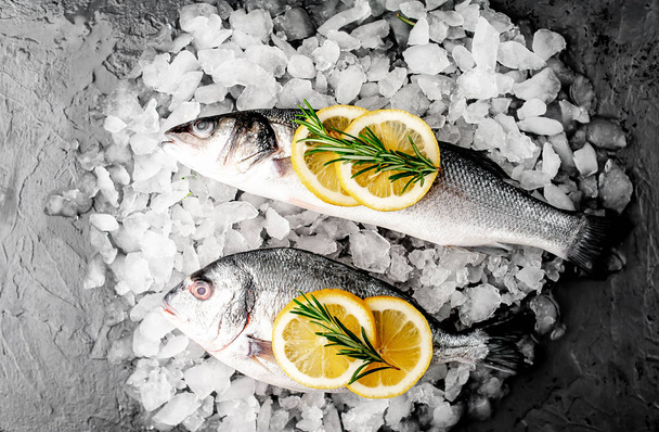 Close View van verse vis met citroen plakjes en rozemarijn op stapel van koud gemalen ijs - Foto, afbeelding