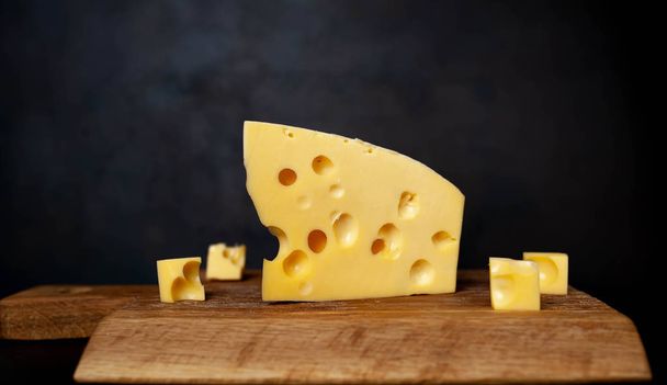 Chunk of Maasdam cheese with pieces on wooden chopping board - Φωτογραφία, εικόνα