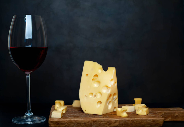 Ahşap tahta üzerinde Maasdam peynirsiyah taş arka plan üzerinde kırmızı şarap ile servis  - Fotoğraf, Görsel