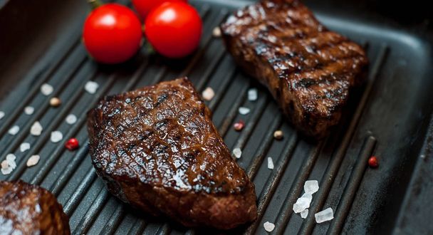 Fresh grilled steaks on grill pan with fresh tomatoes - Fotoğraf, Görsel