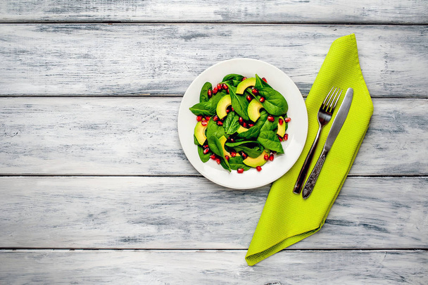 Ensalada verde fresca con hojas de espinaca, rodajas de aguacate y granos de granada sobre mesa de madera
  - Foto, Imagen