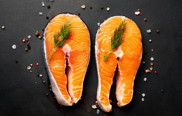 Fresh raw salmon steaks with spices and dill on black stone background - Photo, Image