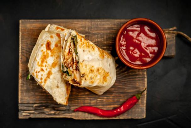 Burrito tradicional mexicano envuelto con pollo y verduras con salsa picante sobre tabla de cortar de madera
  - Foto, imagen