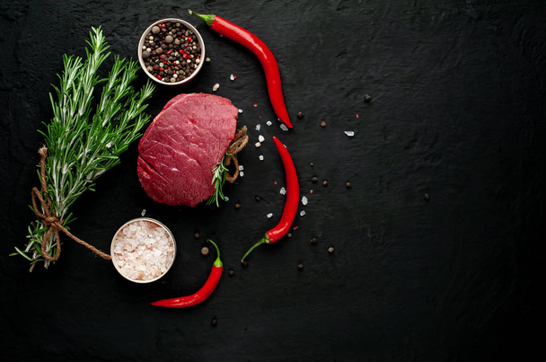 Rauwe biefstuk met groene rozemarijn twijgen en specerijen op zwarte stenen achtergrond  - Foto, afbeelding