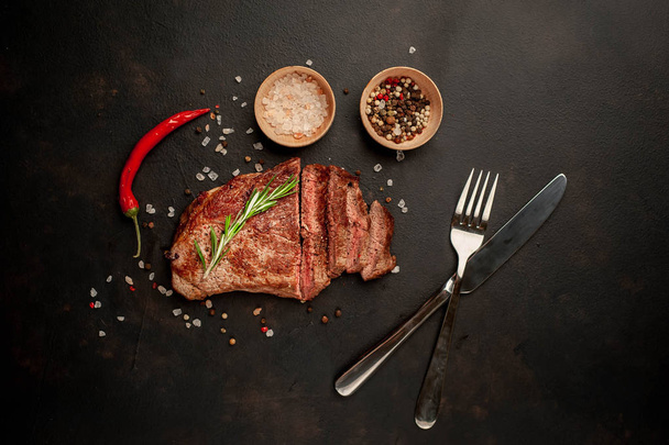 Fresh grilled pork steak with spices and rosemary twig on black stone background - Photo, Image