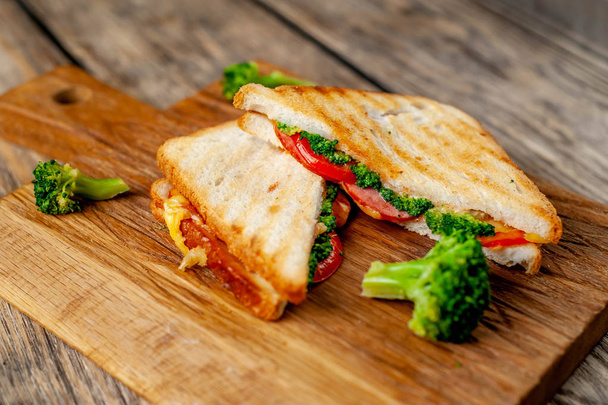 Sandwiches frescos a la parrilla con jamón, brócoli fresco y queso sobre tabla de cortar de madera
 - Foto, Imagen