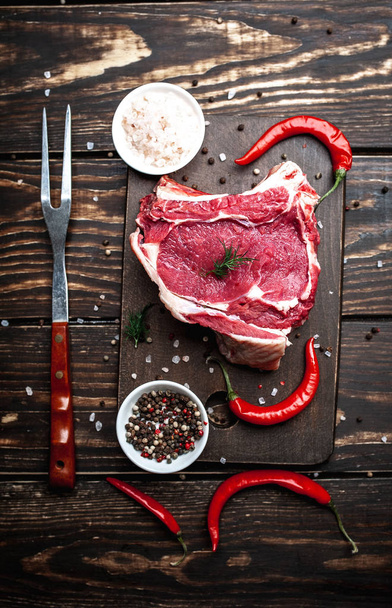 Raw fat pork steak with spices and hot chili peppers on wooden chopping board  - Photo, Image