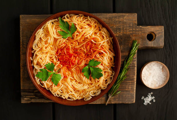 macarrão de espaguete italiano com molho de tomate e folhas de salsa no fundo de pedra escura
 - Foto, Imagem