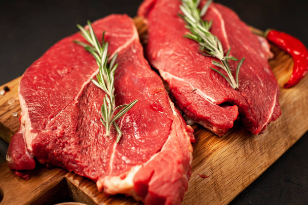 Rauw rundvlees steaks met specerijen en rozemarijn op stenen achtergrond - Foto, afbeelding