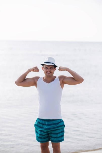 Happy man show his biceps in front of sea. Young man walking on the beach - Photo, image