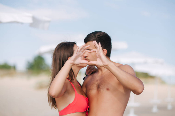 Το ευτυχισμένο ζευγάρι κάνει καρδιά. Γυναίκα και άντρας στην παραλία. Φιλιούνται. - Φωτογραφία, εικόνα