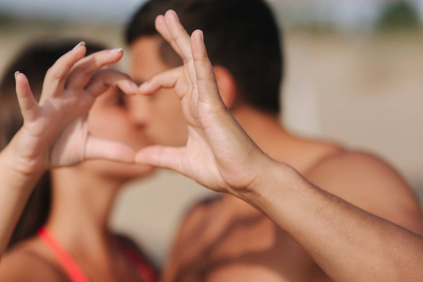 glückliches junges Paar küsst sich und macht ein Herz an den Händen. Paar zu Fuß am Strand. Liebe - Foto, Bild