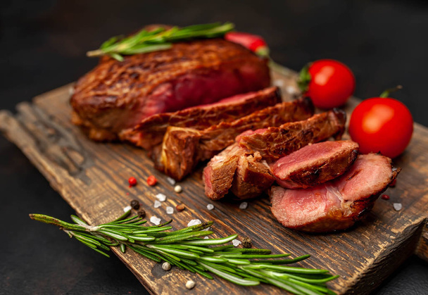 Ahşap doğrama tahtası üzerinde biberiye dalları ile dilimlenmiş orta nadir sığır eti biftek yakın görünümü - Fotoğraf, Görsel
