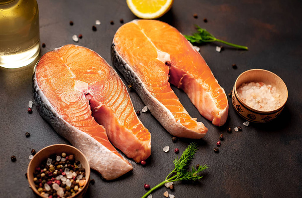 Fresh raw salmon steaks with spices and lemon on black stone background - Photo, Image