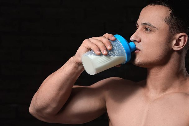 Sporty man drinking protein shake on dark background - Photo, Image