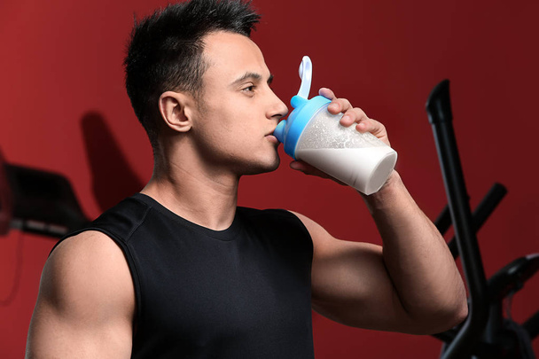Sporty man drinking protein shake on color background - Photo, Image
