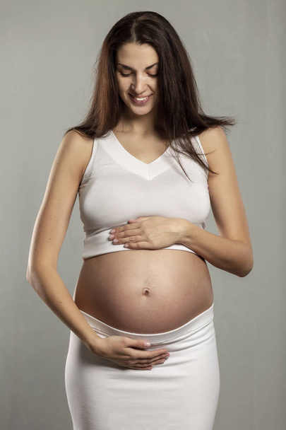 Young beautiful pregnant woman gently hugs belly and smiles - Foto, afbeelding