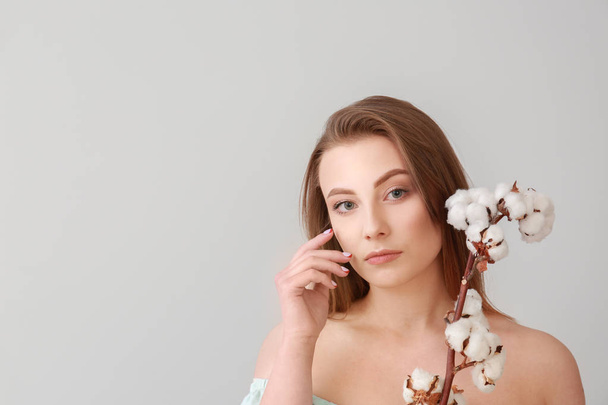 Beautiful young woman with cotton branch on light background - Photo, image